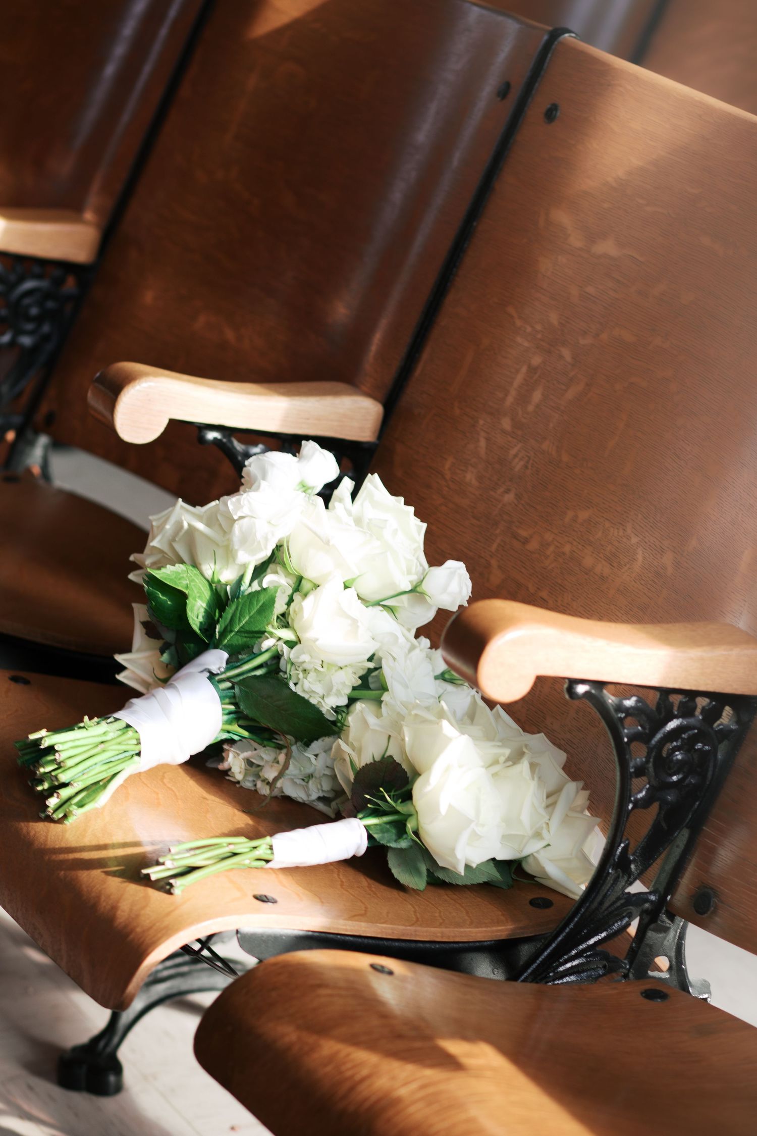 A classic white rose wedding bouquet rests on a wooden theater-style seat.