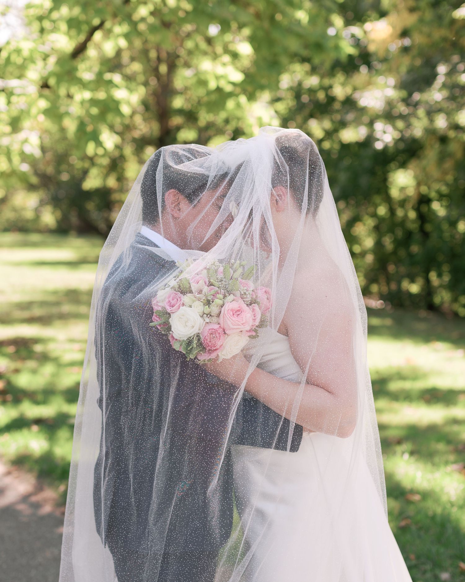 A romantic moment captured through a white wedding veil with pink roses in the foreground.