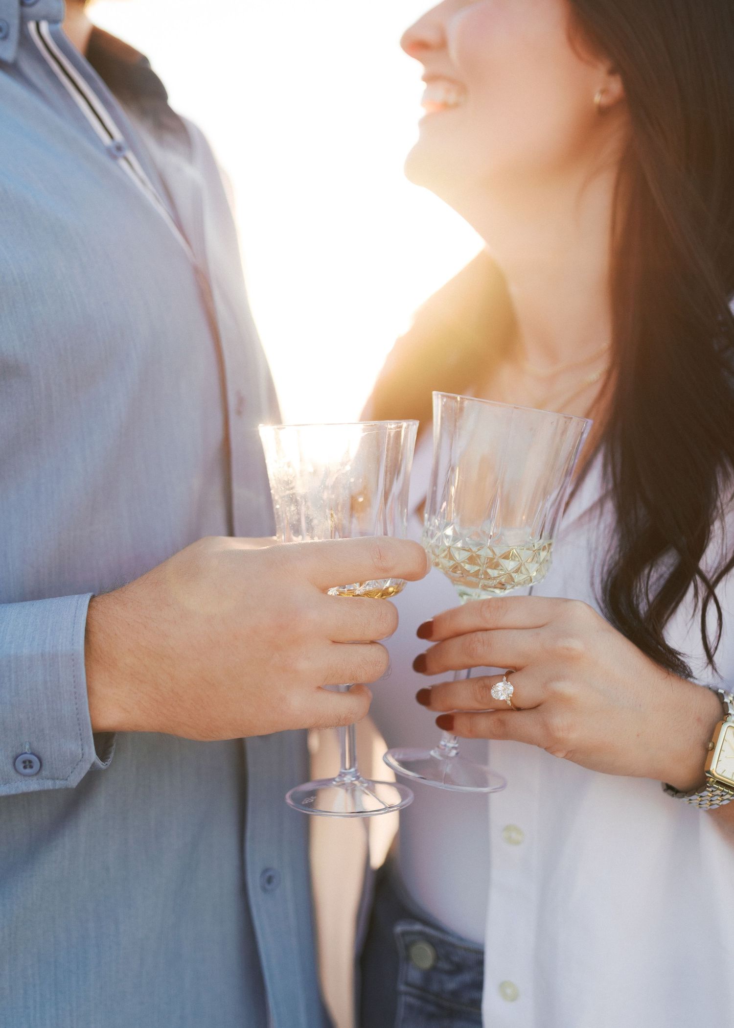 Two people hold champagne glasses together in romantic sunset lighting.