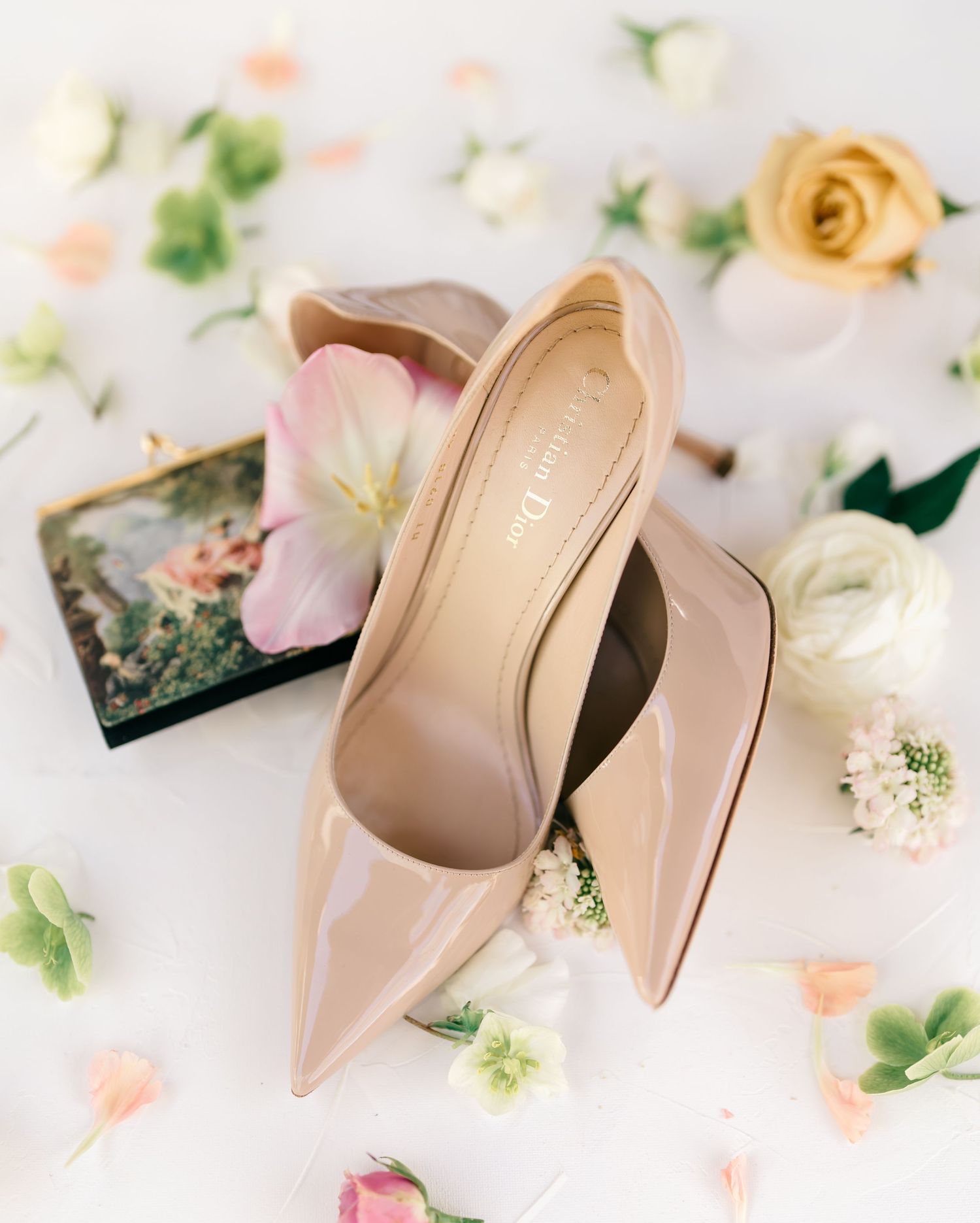 Elegant nude high heel shoes arranged with delicate pink and peach roses and floral elements on a light background.