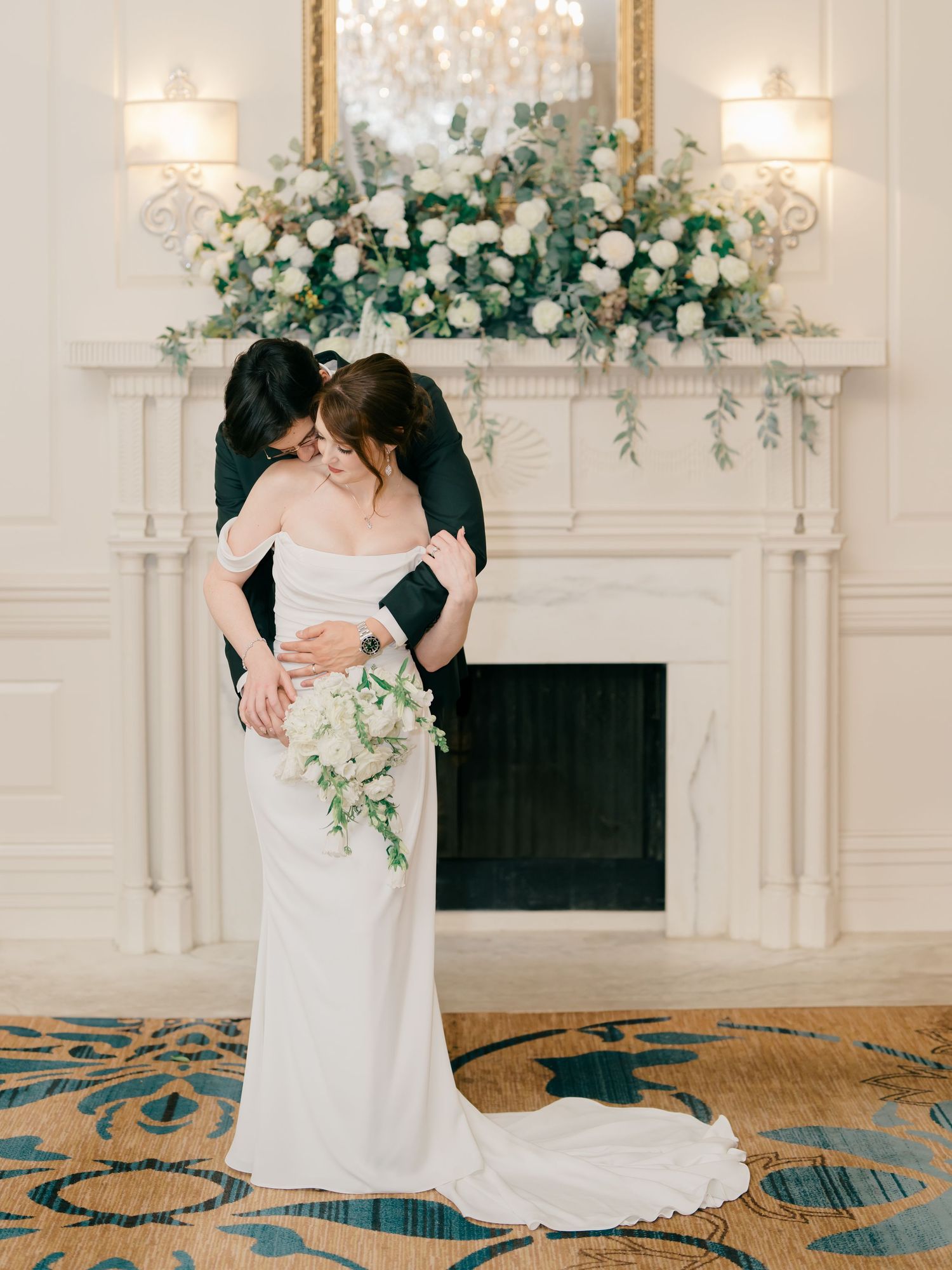 Elegant couple in white wedding attire share an intimate dance moment on an ornate blue and gold patterned ballroom floor.