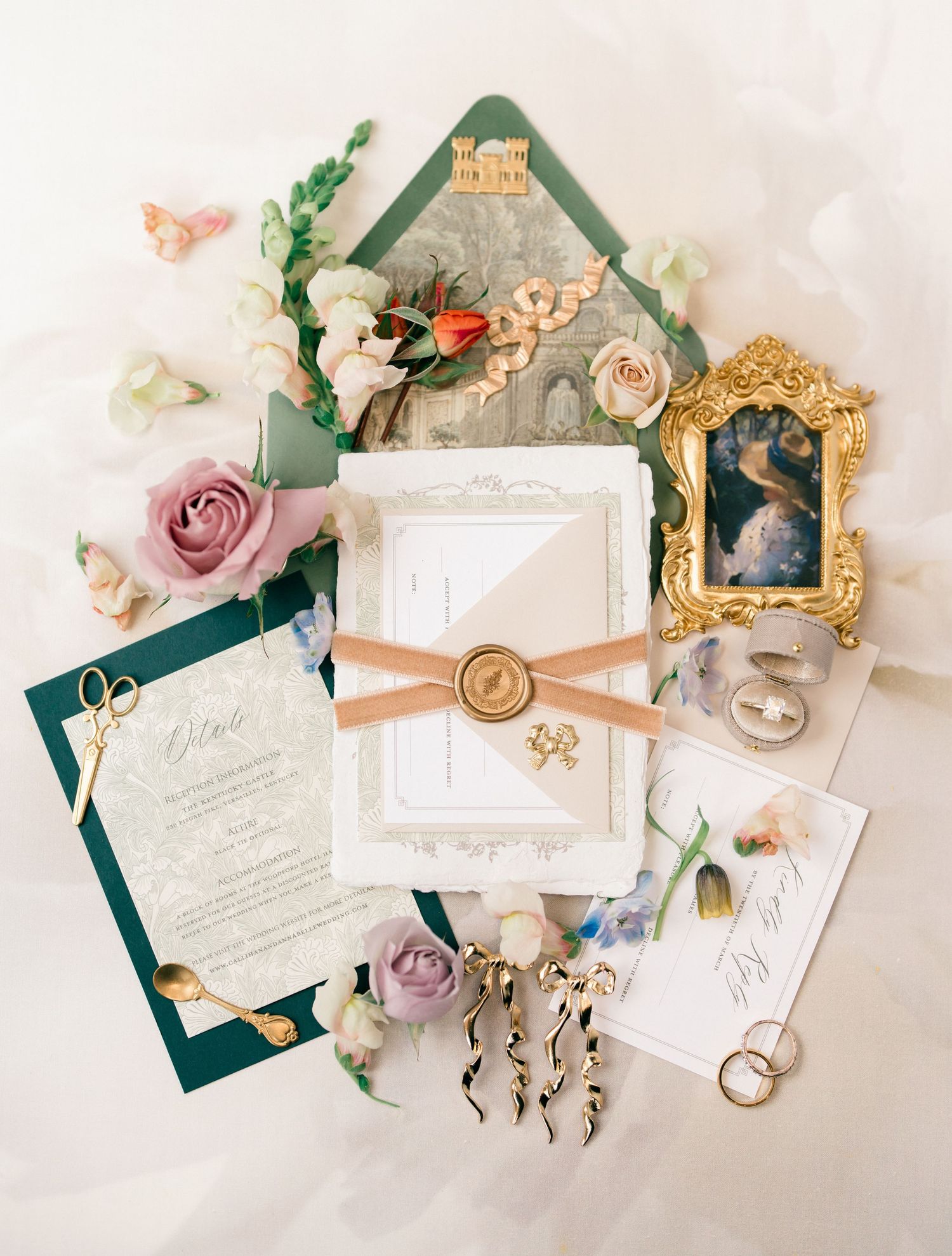 Wedding stationery flat lay with elegant floral designs, vintage details, and emerald green ribbons on a light pink background.
