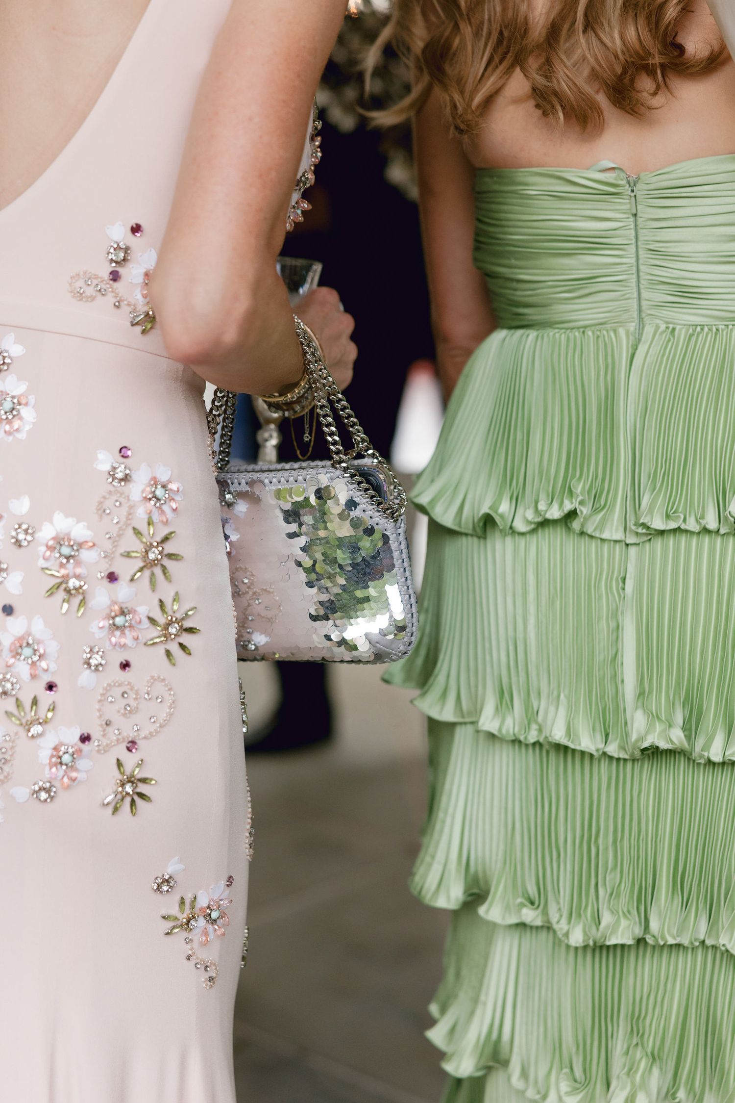 Two formal dresses at an event - one in pale pink with floral beading and one in mint green with tiered ruffles.