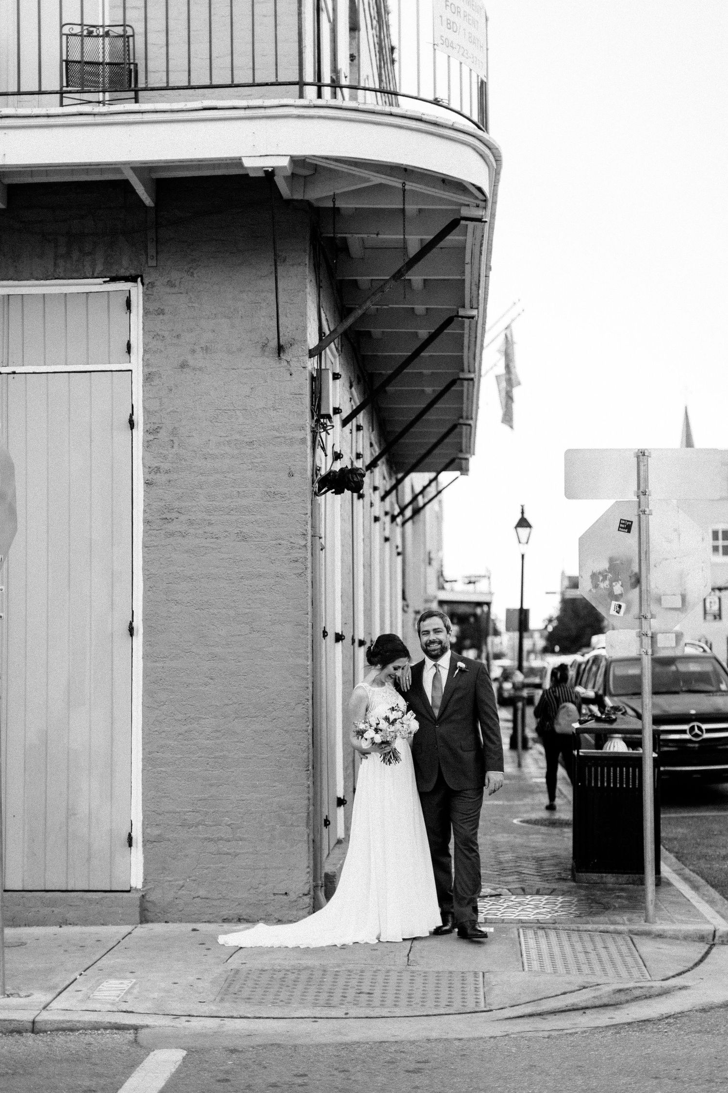 A couple stands on a corner of a historic building with a wrap-around balcony in the French Quarter of New Orleans.