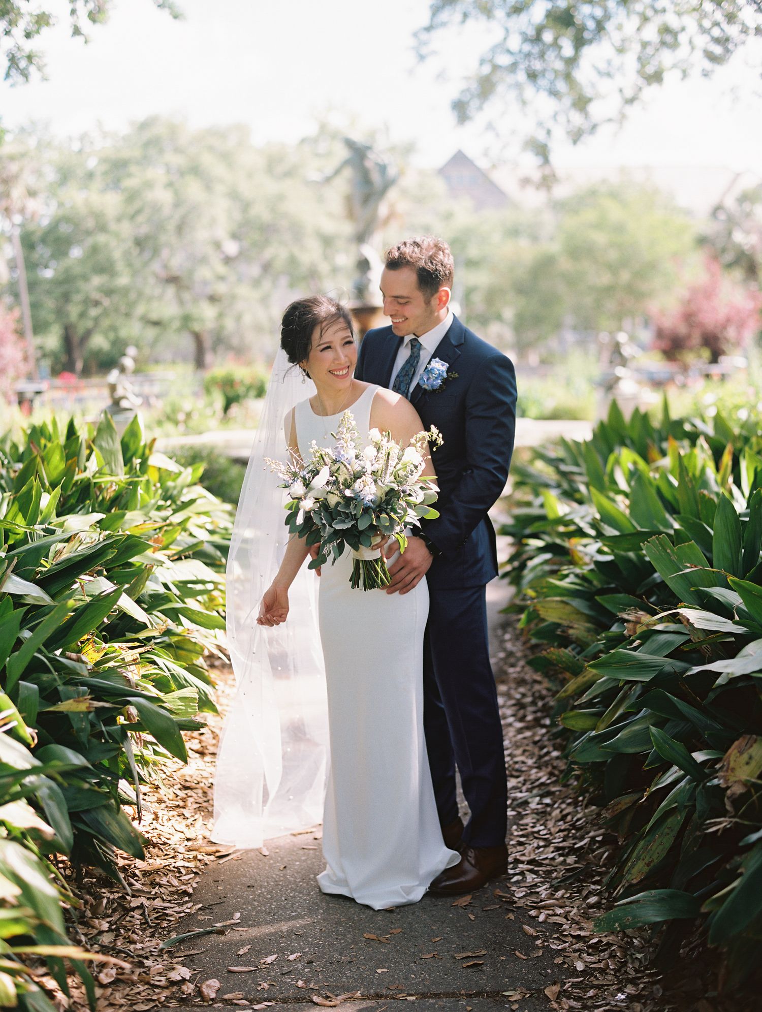 A couple shares romantic moments in a garden setting with lush greenery and natural sunlight at Audobon Park in the Garden District
