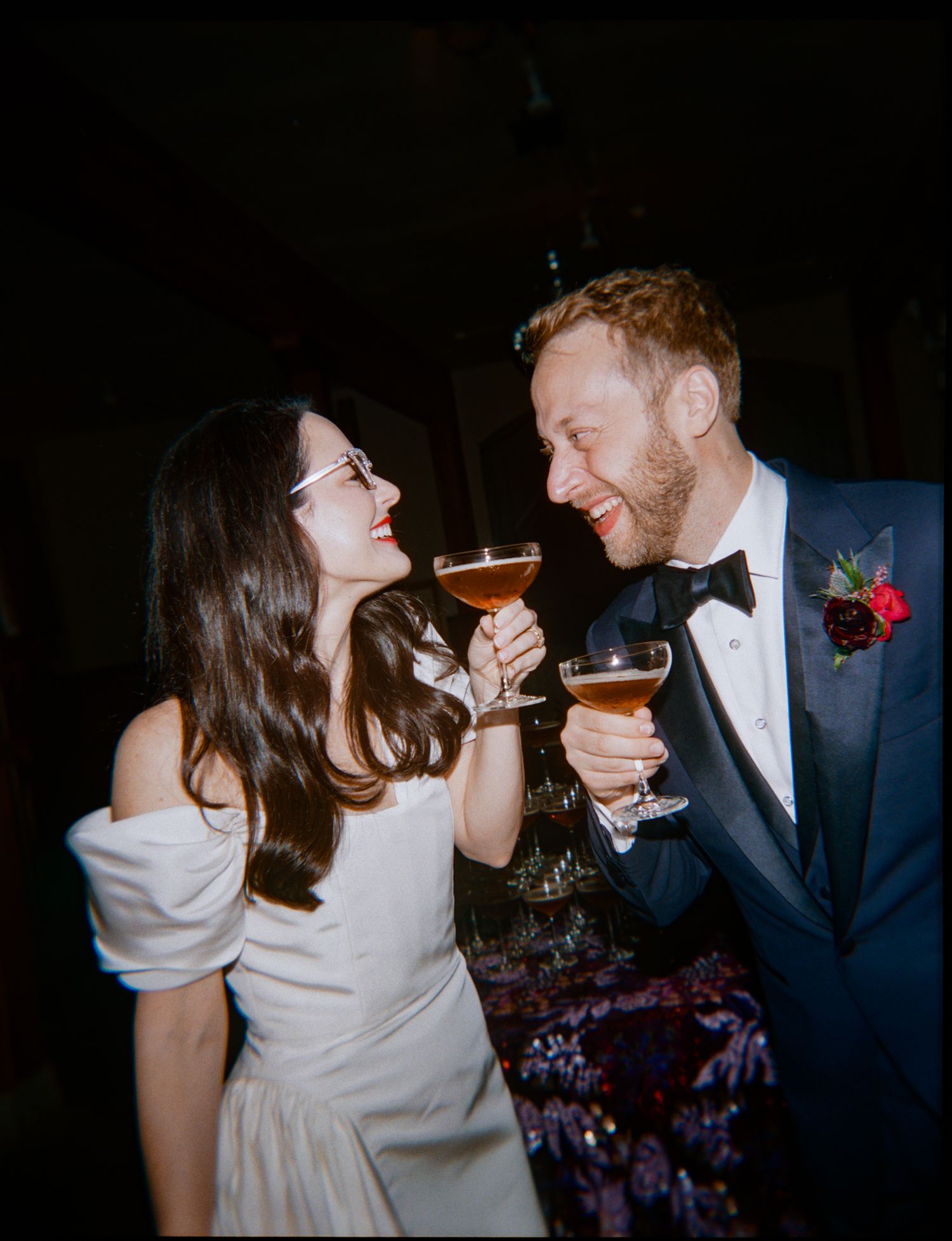 A couple shares a romantic moment laughing together while holding cocktail glasses at a formal evening event.