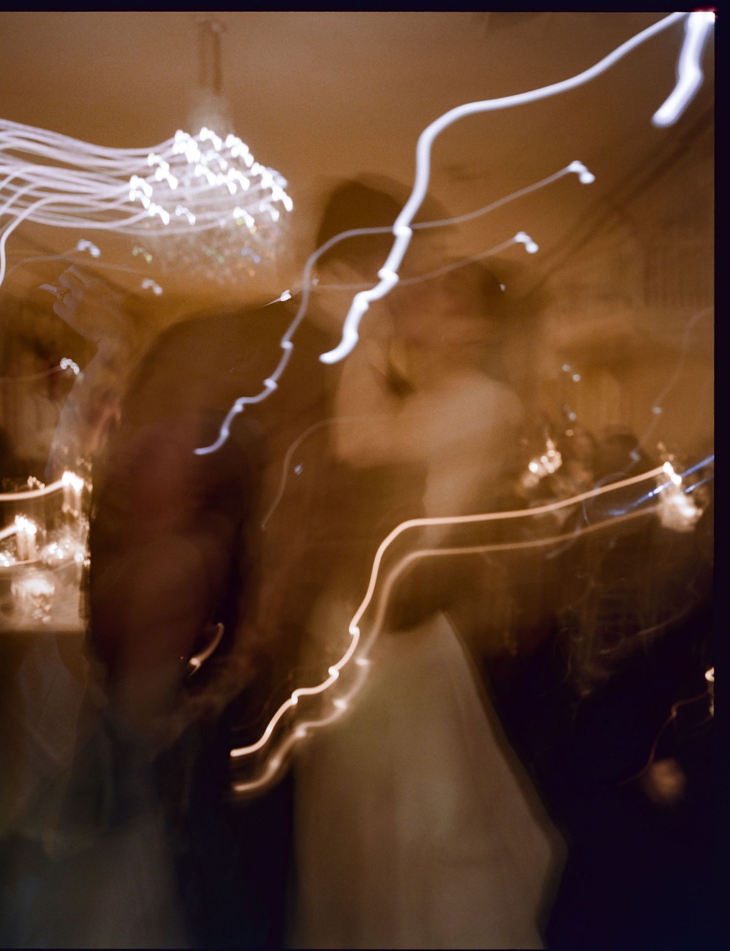 Abstract light trails create wavy white streaks against a dark brown background in a long exposure photograph.