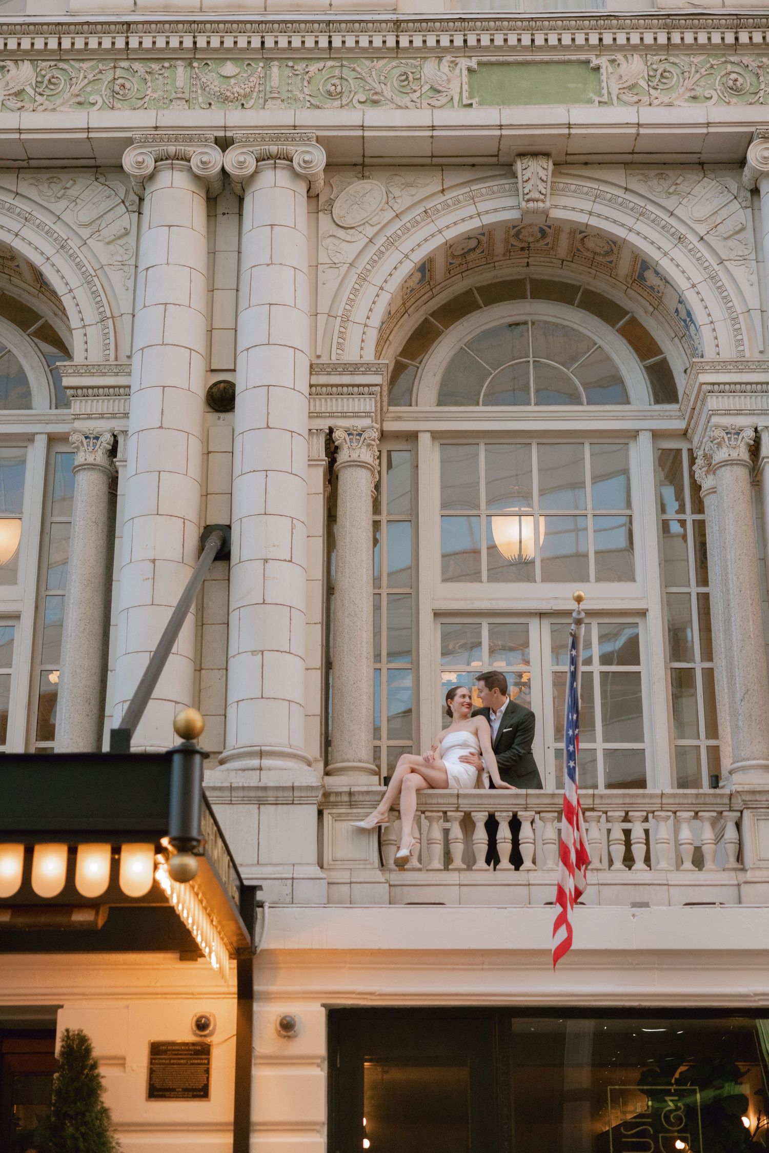 Elegant couple poses on ornate balcony of The Hermitage Hotel in Nashville, TN with classical architecture and decorative lighting below.