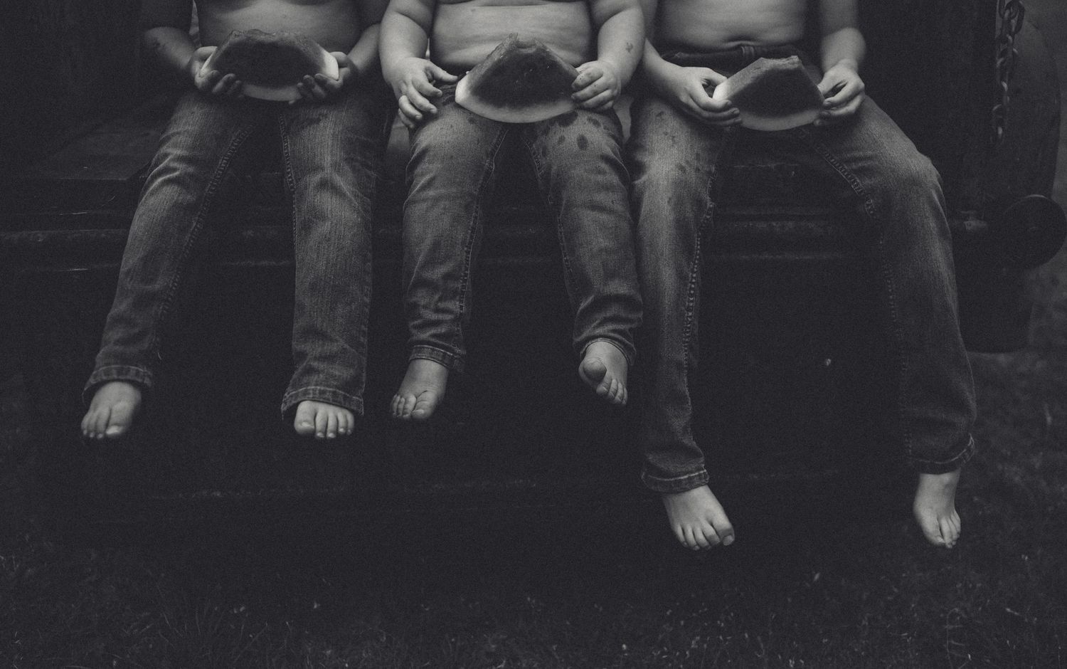 Black and white photo of three pairs of bare feet wearing cowboy hats.