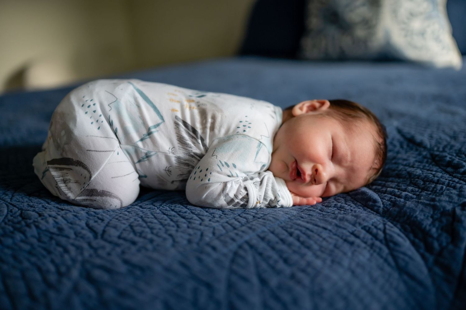 Sleeping baby in white onesie on blue textured bedding.