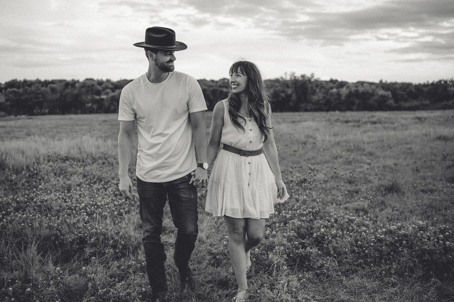 Black and white portrait of couple standing together in grassy field.