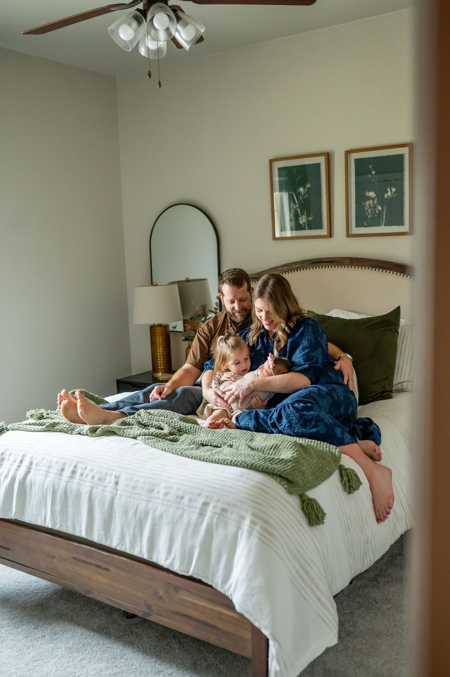 Family spending quality time together on bed with green throw blanket and decorative wall art.