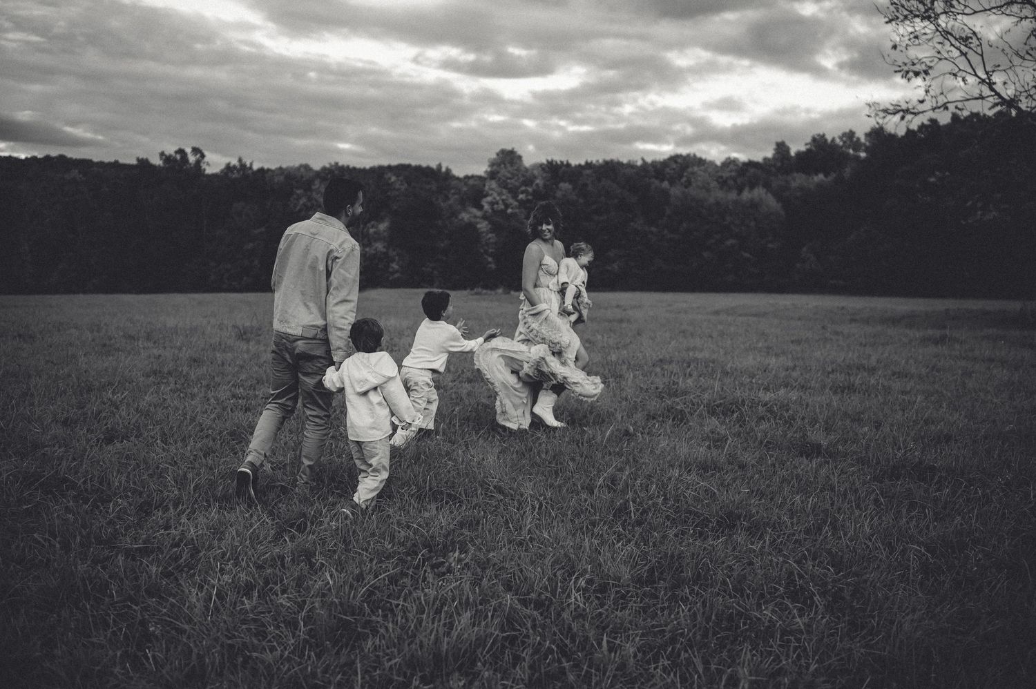 Black and white photo of family playing in open field under cloudy sky.