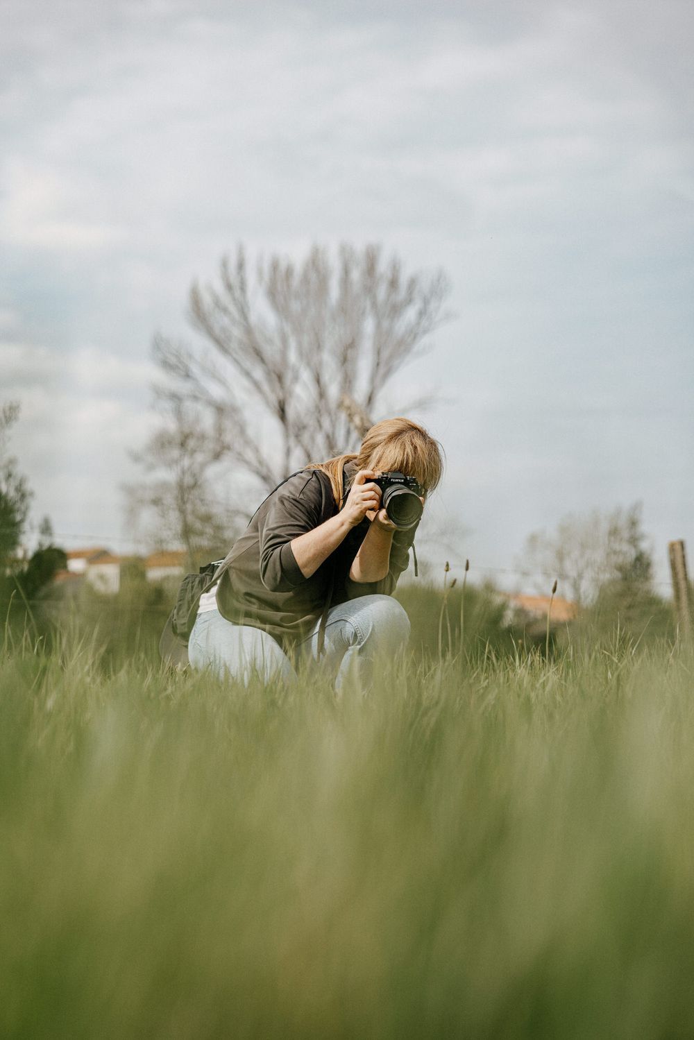 Photographer crouching in tall grass taking pictures on an overcast day.