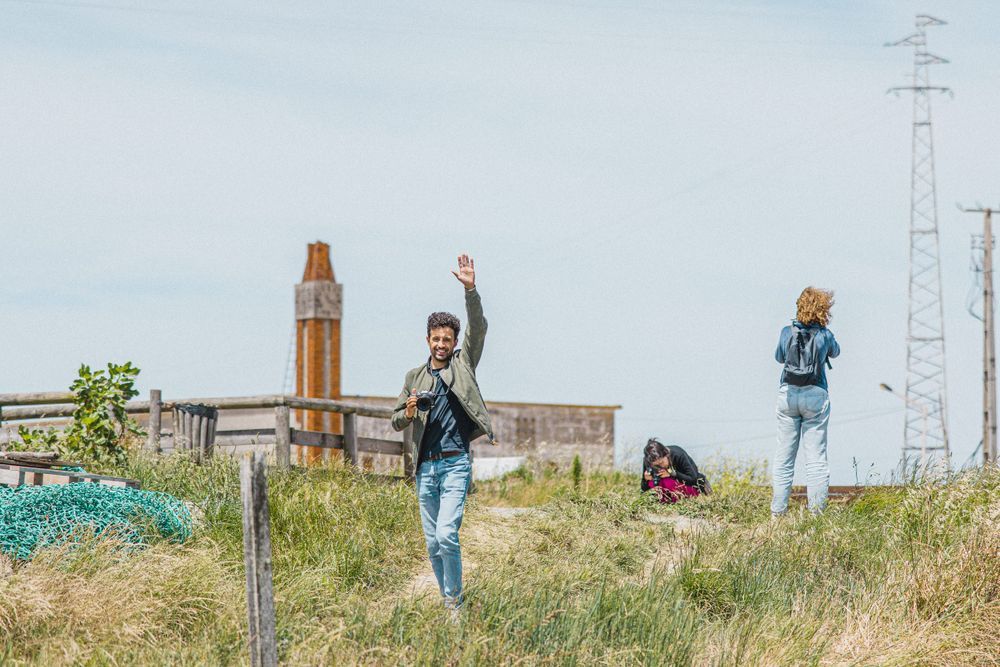 Group enjoying sunny day on grassy hill with industrial buildings in background.