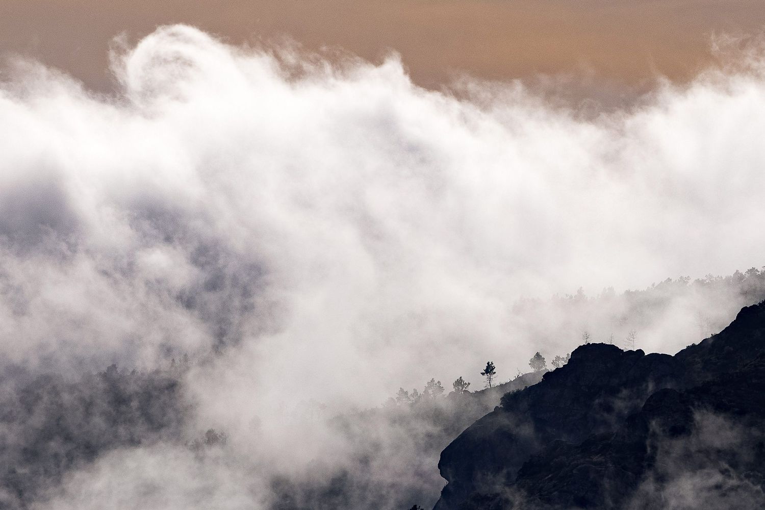 Misty clouds rolling over dark mountain peaks in dramatic lighting.