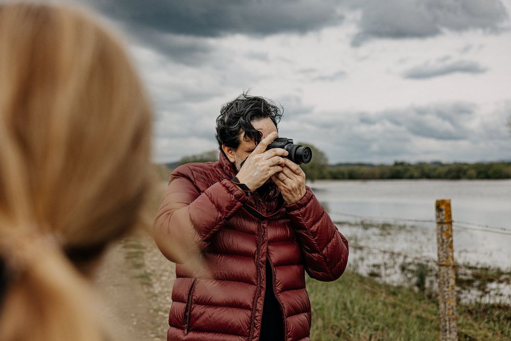 Photographer in red puffer jacket taking pictures by a lake on an overcast day.