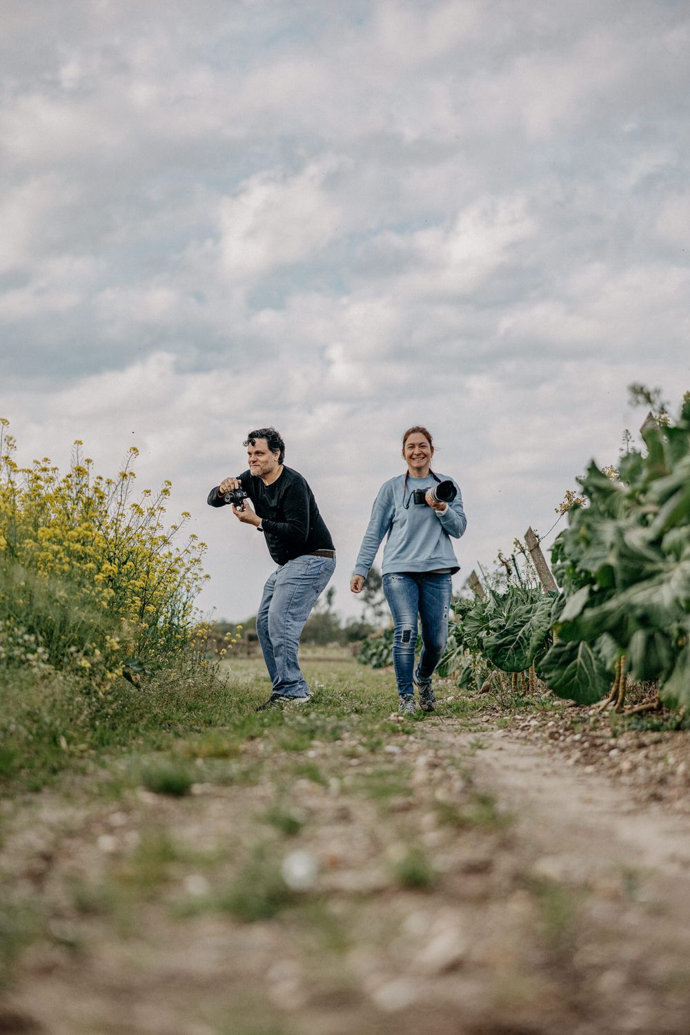 Two photographers running down a nature trail with cameras in hand under cloudy skies.