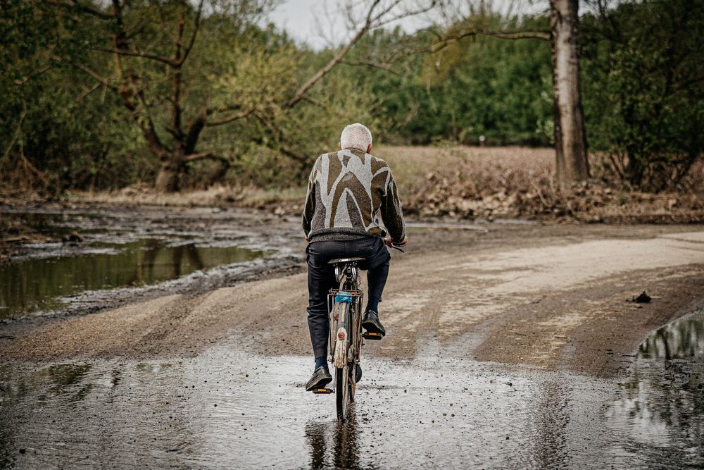 Cyclist riding through puddles on a wet path surrounded by trees.