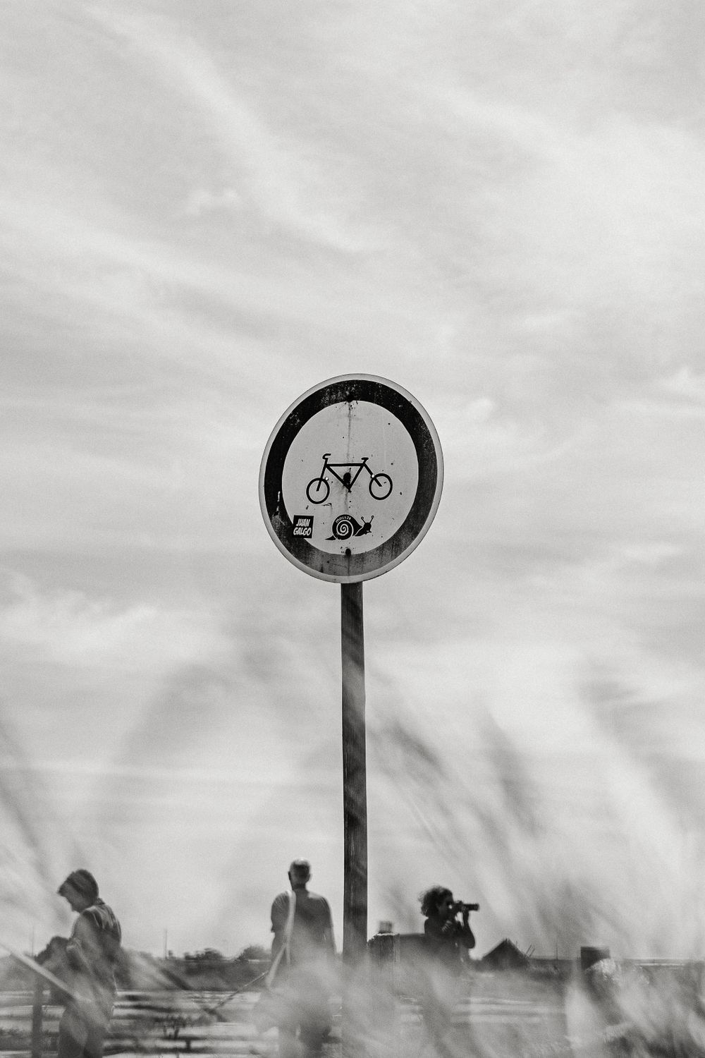 Black and white image of a bicycle prohibition sign with silhouettes in the background.