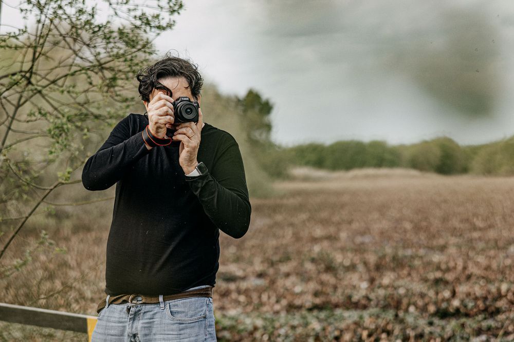 Photographer in dark clothing taking pictures in a natural setting.