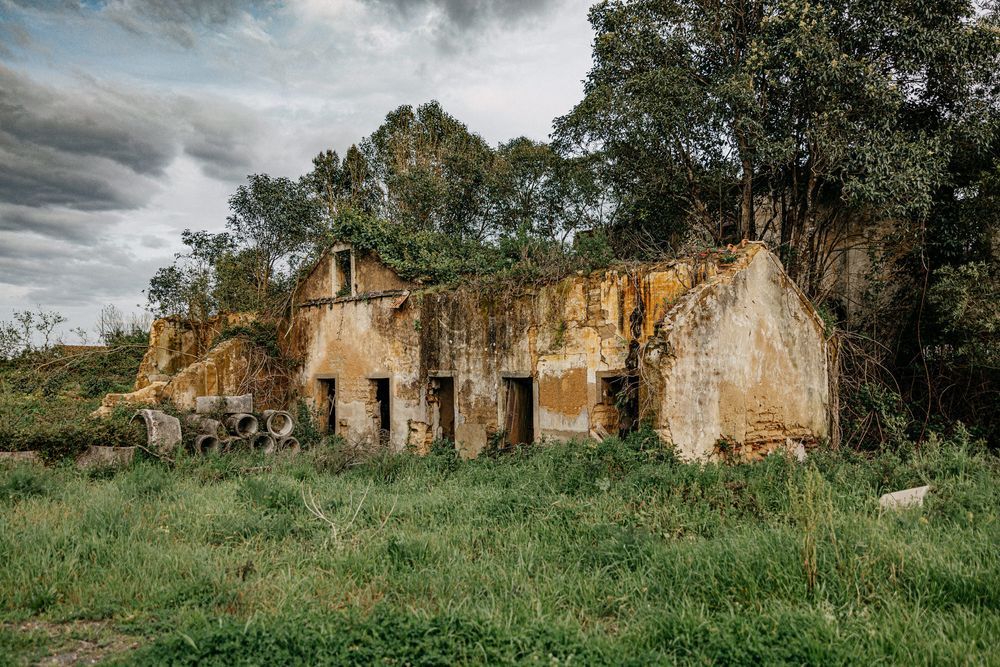 Abandoned rustic building ruins with crumbling walls in grassy field.