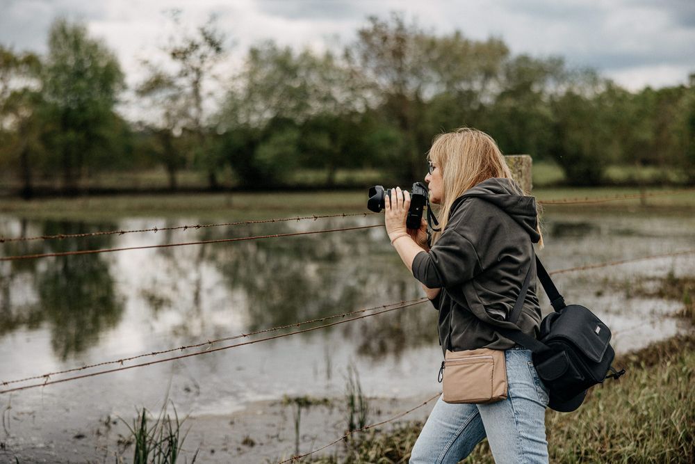 Nature photographer with camera capturing wildlife shots near a reflective lake.
