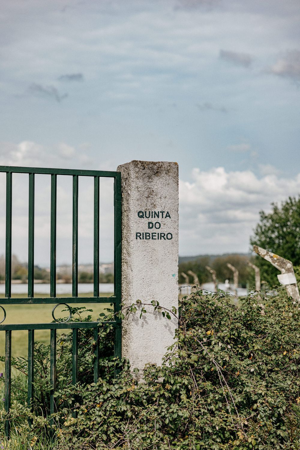 Stone gate post marked 'Quinta do Ribeiro' stands against a cloudy sky in a rural setting.