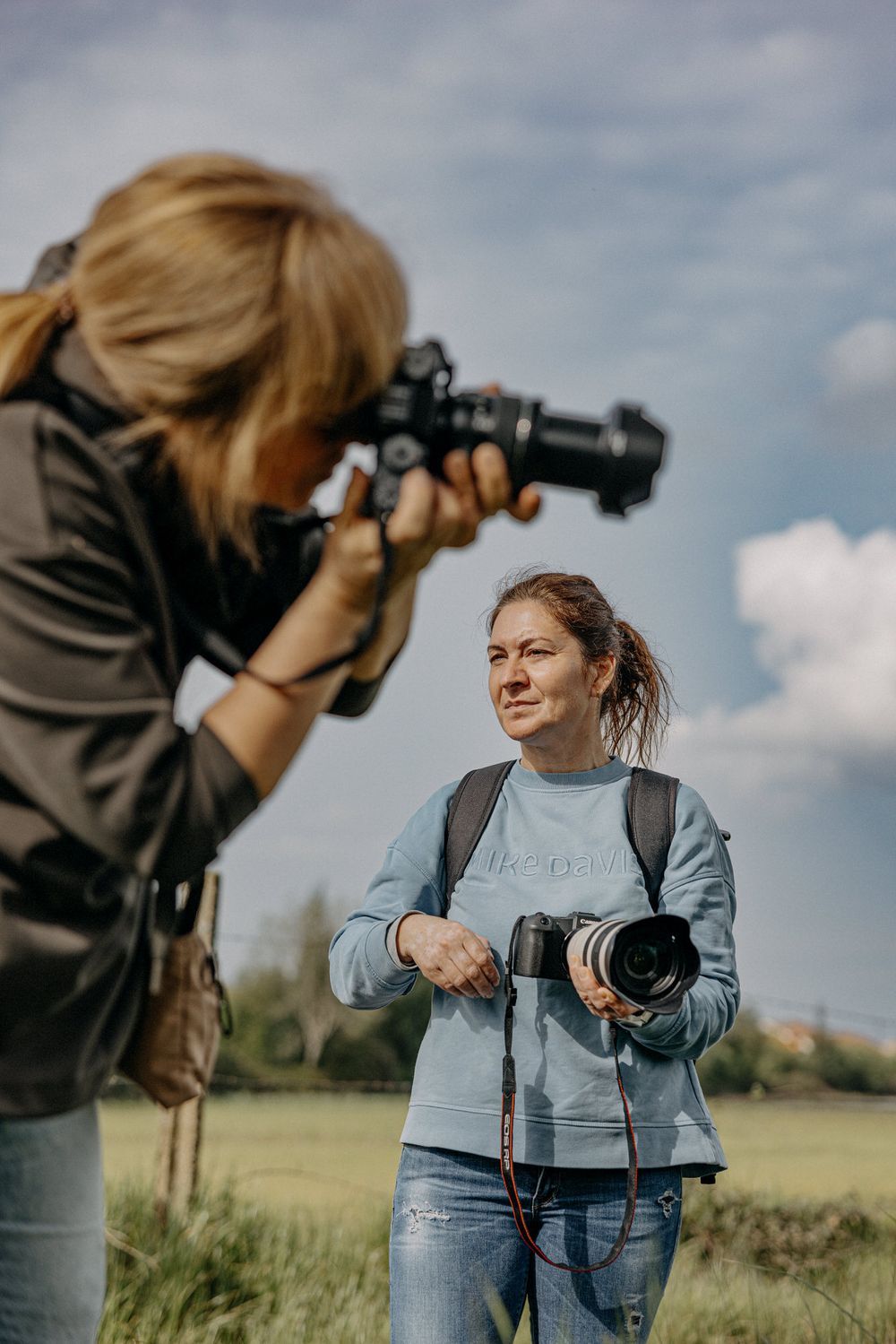 Two photographers with professional cameras practicing photography techniques in a field.