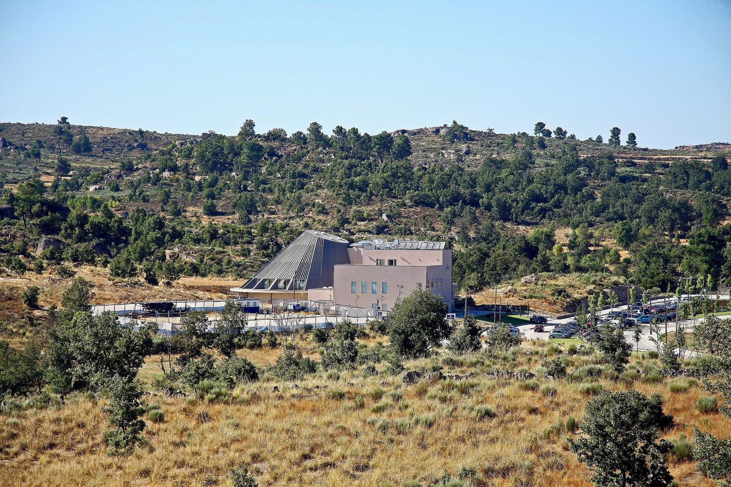 Large building complex nestled in arid hills with scattered vegetation.