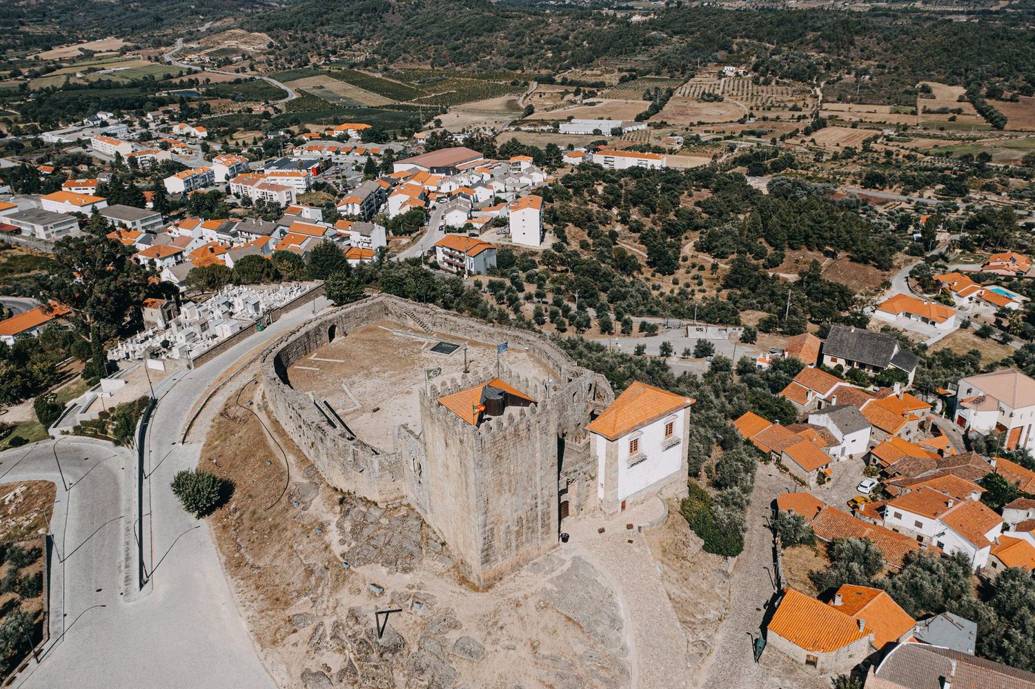 Aerial view of a medieval fortress and white buildings with orange roofs in a Portuguese village.