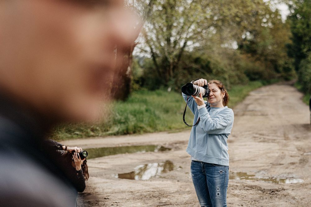 Photographers capturing scenes on a muddy dirt path with puddles and trees in the background.