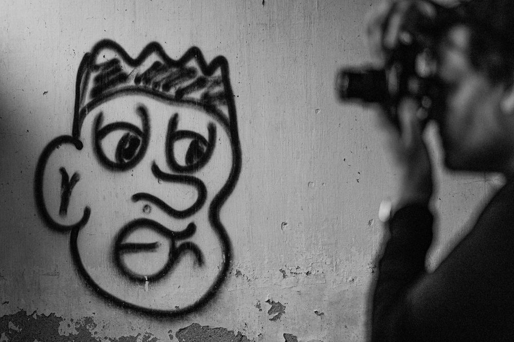 Black and white street art showing cartoon face with crown while photographer takes picture.