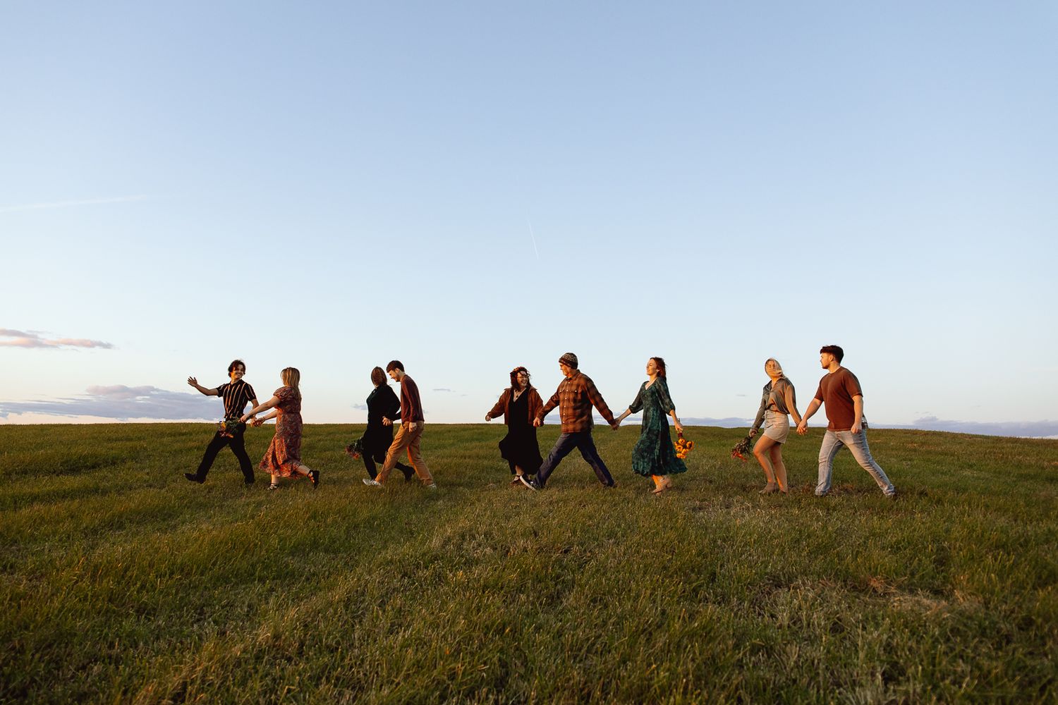 family of nine walking and holding hands on a hill with a blue sky in the background