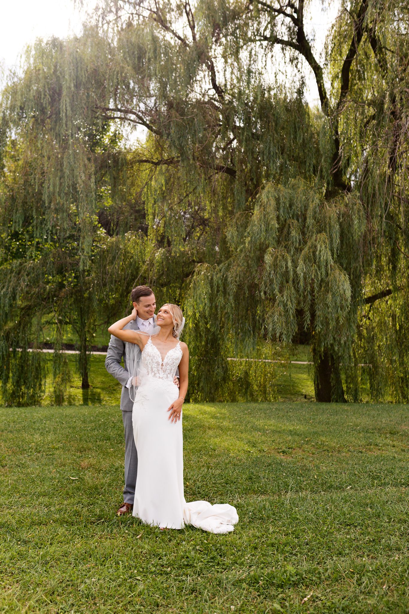 bride with her hand on grooms neck to pull him in for a kiss under willow trees