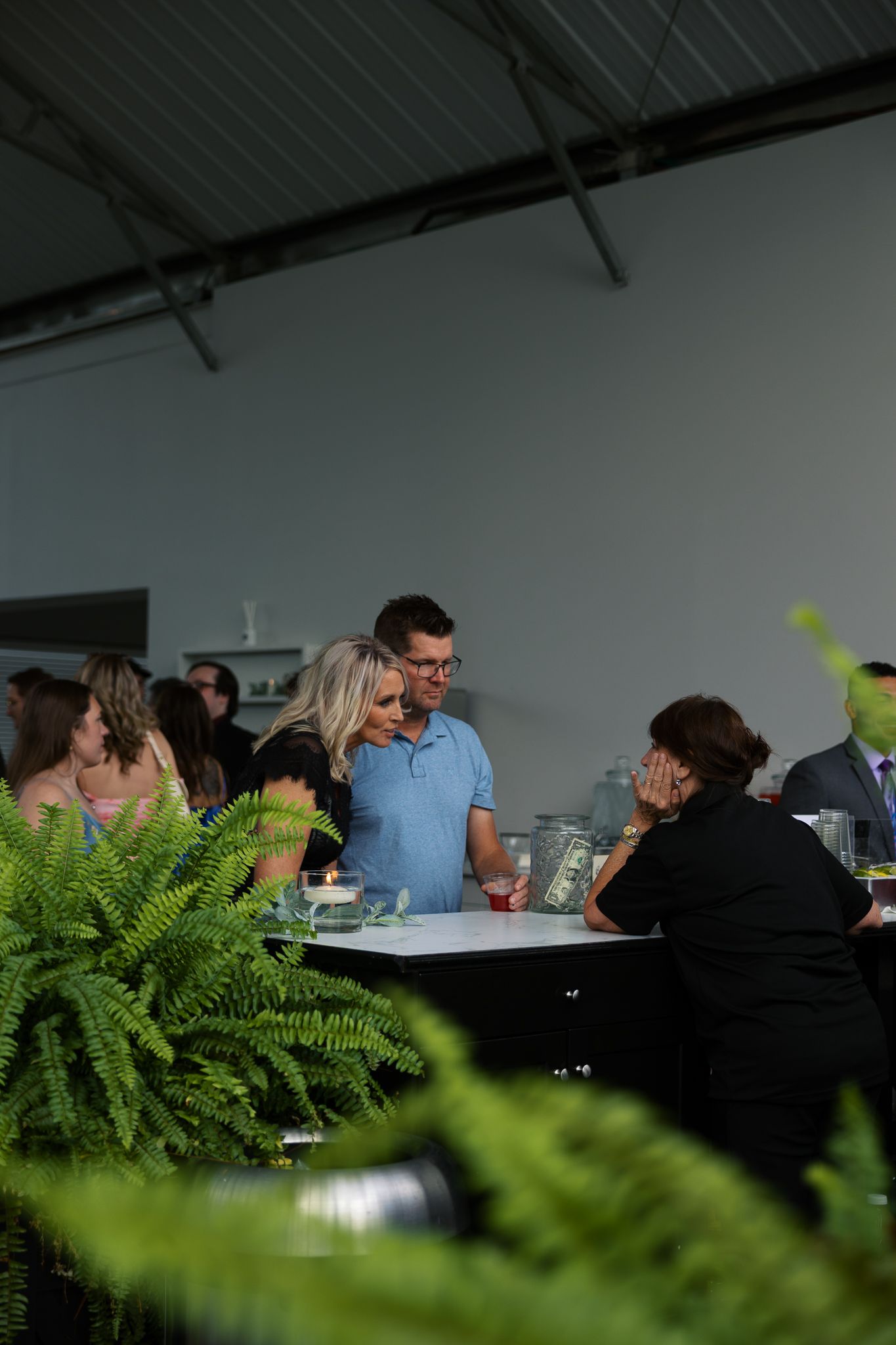 candid shot through ferns of wedding guests choosing their drinks at the bar during cocktail hour