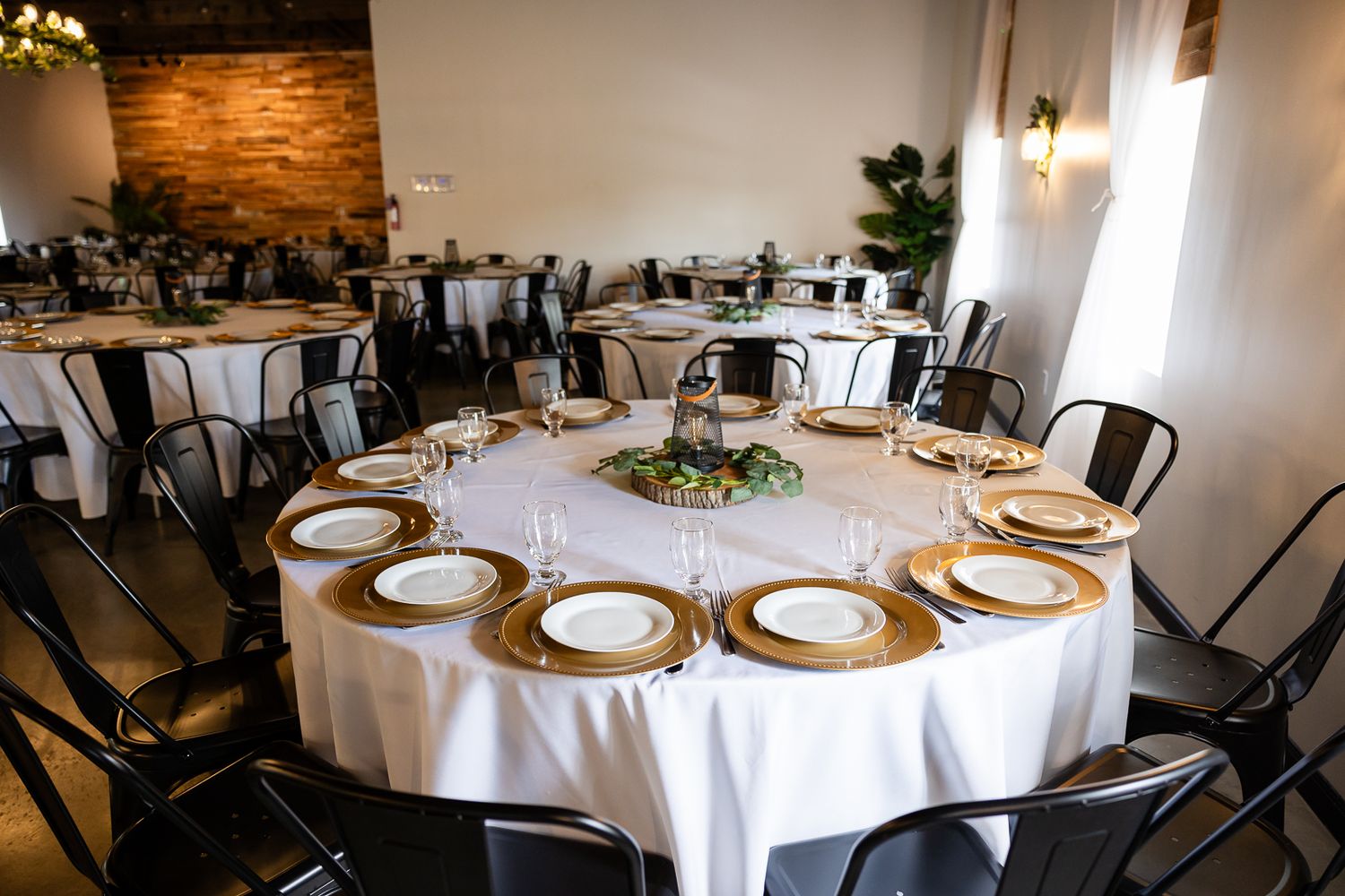 indoor table setting for reception with black chairs, white tablecloths, and gold chargers