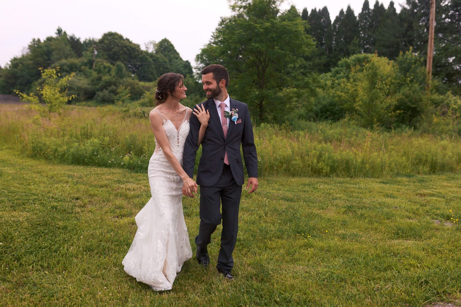 bride and groom walking together in a field while holding hands