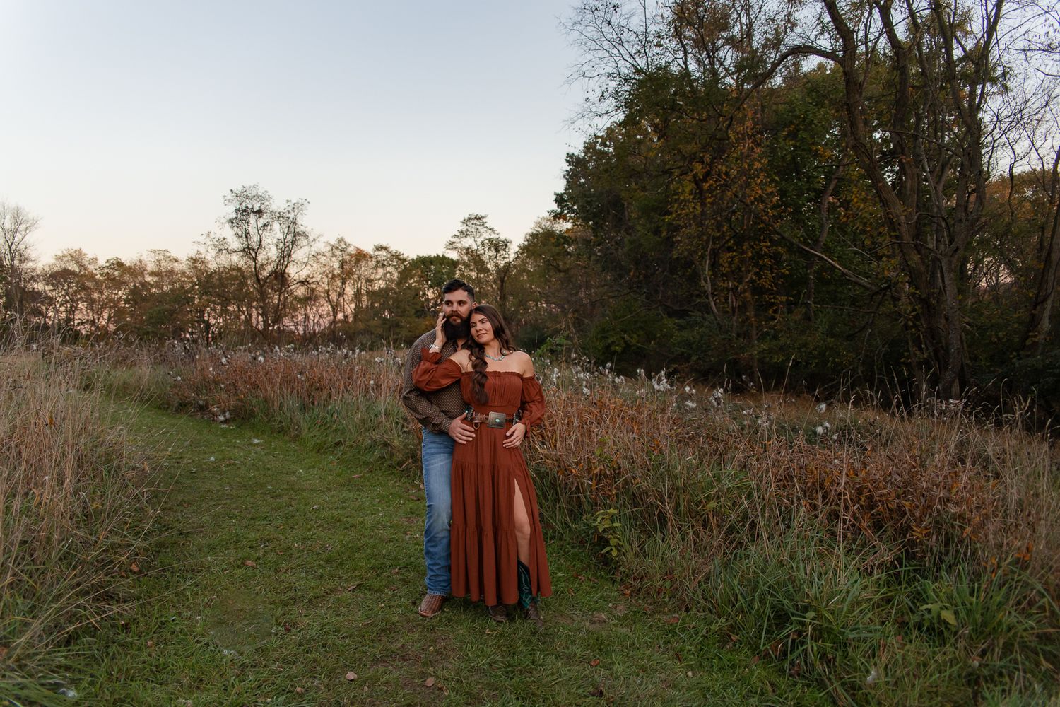 woman in rust red dress standing in front of man with her right hand on his cheek