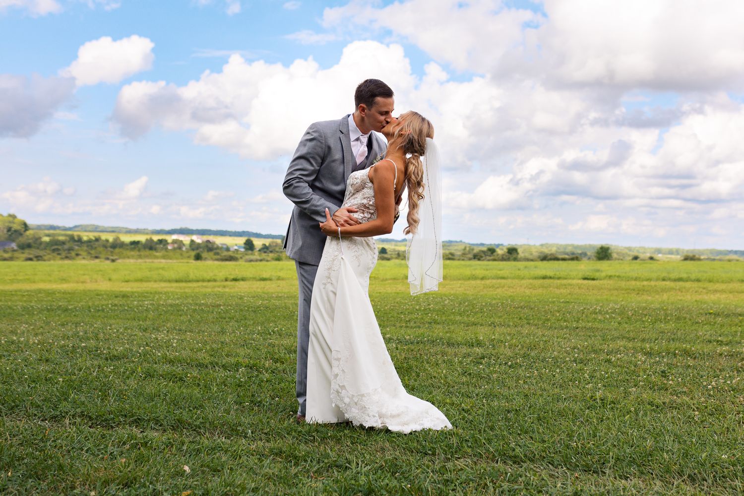man and woman kissing in suit and wedding dress under a perfect blue sky with fluffy white clouds