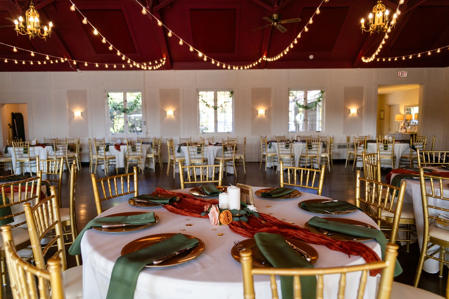 gold chairs set around white round tables with green and rust accents below twinkle lights