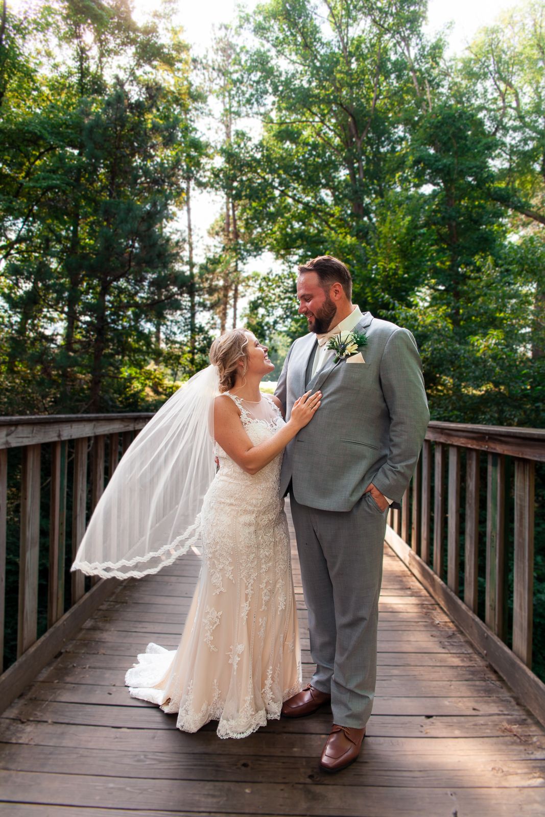 man and woman standing on wooden bridge with her arm on his chest while they look at each other