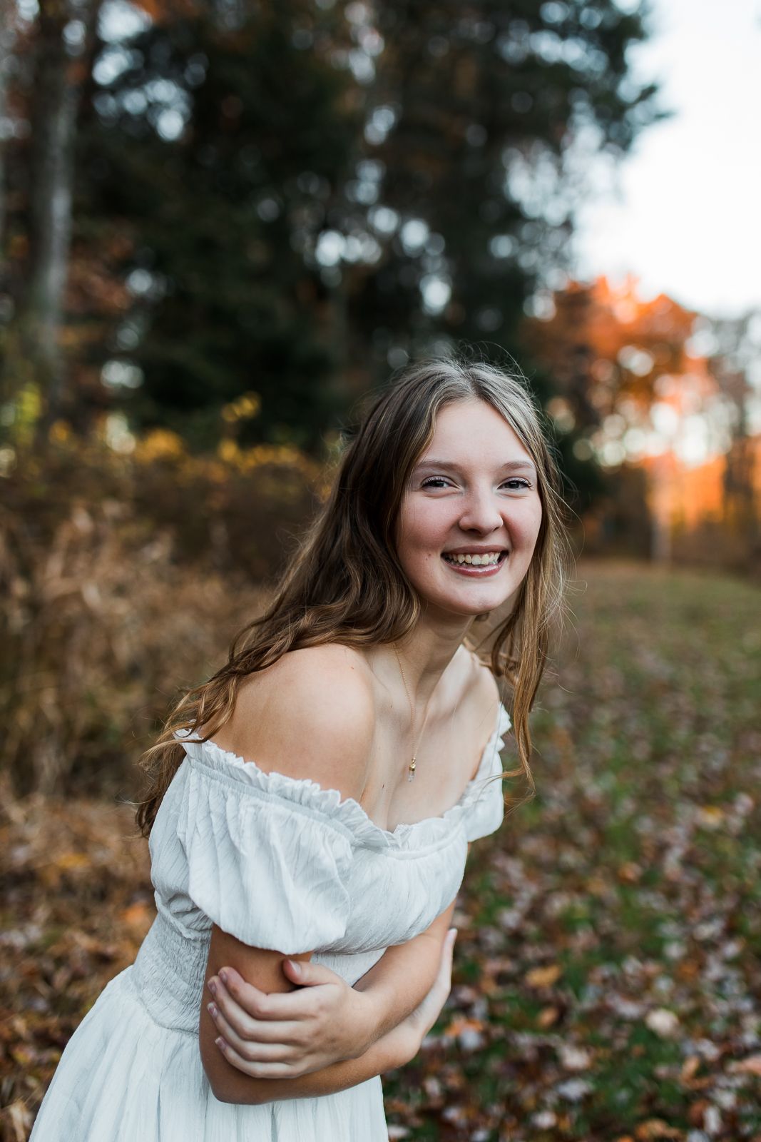 brunette girl smiling really big while wearing a white dress in the fall
