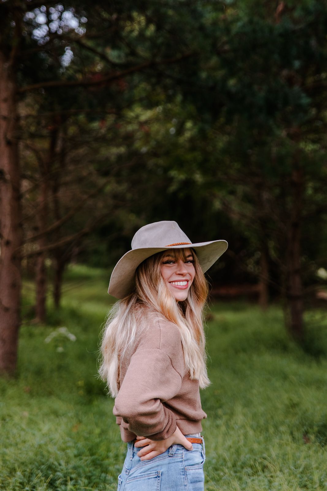 woman with a beautiful smile looking over her shoulder while wearing a brown sweater and tan stylish hat