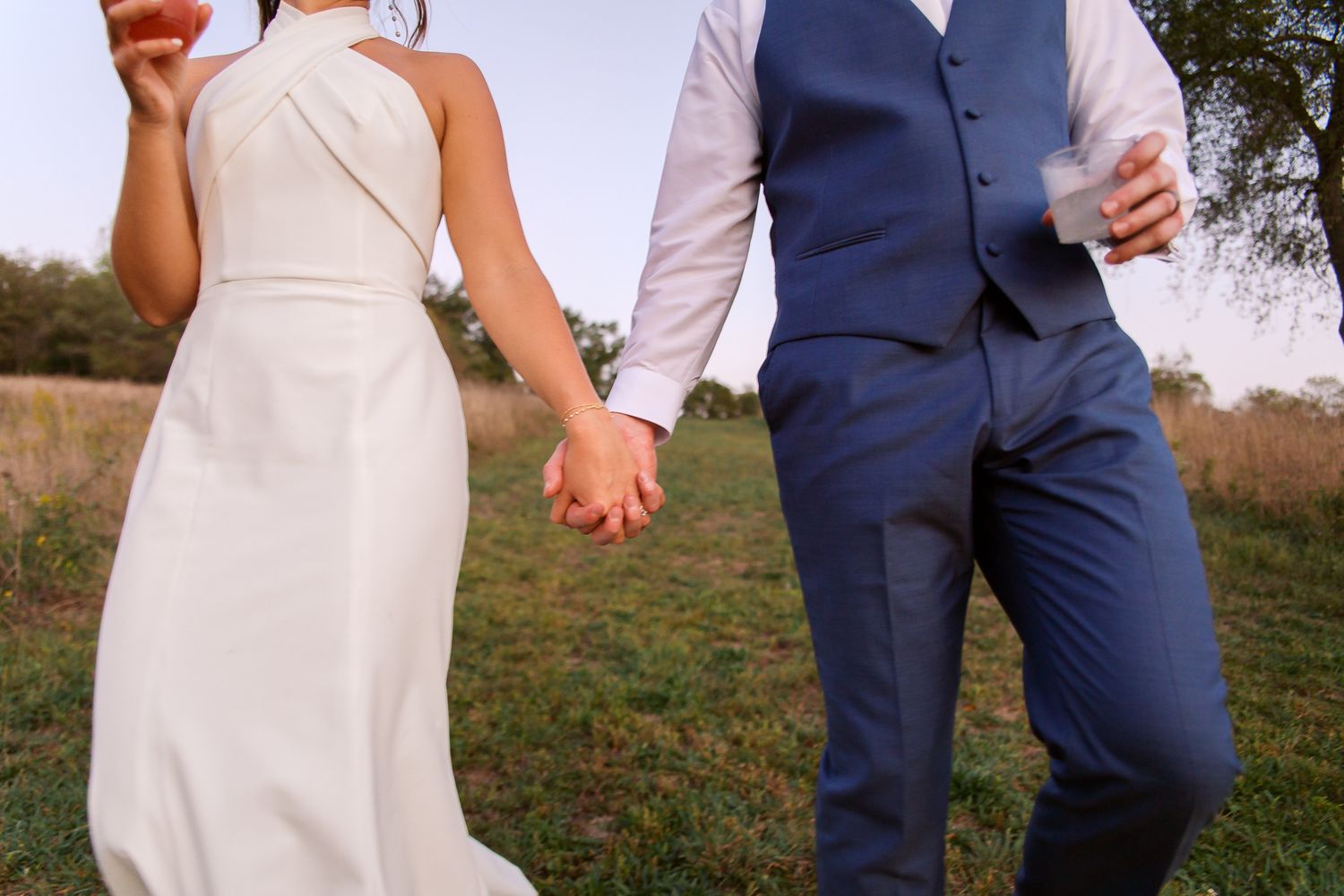 bride and groom holding hands walking with drinks in hand