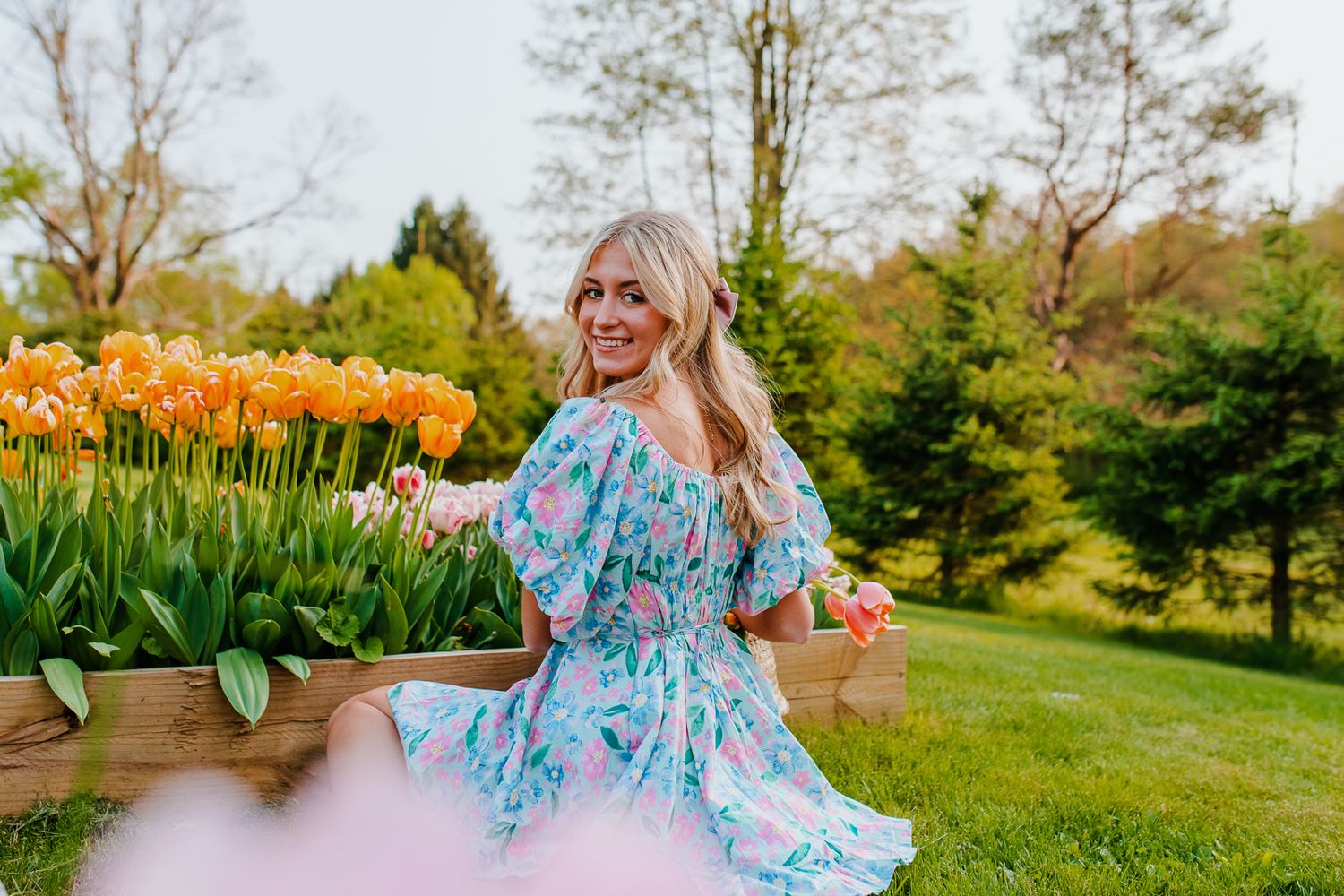 girl with blonde hair in a blue floral dress looking over her shoulder and smiling