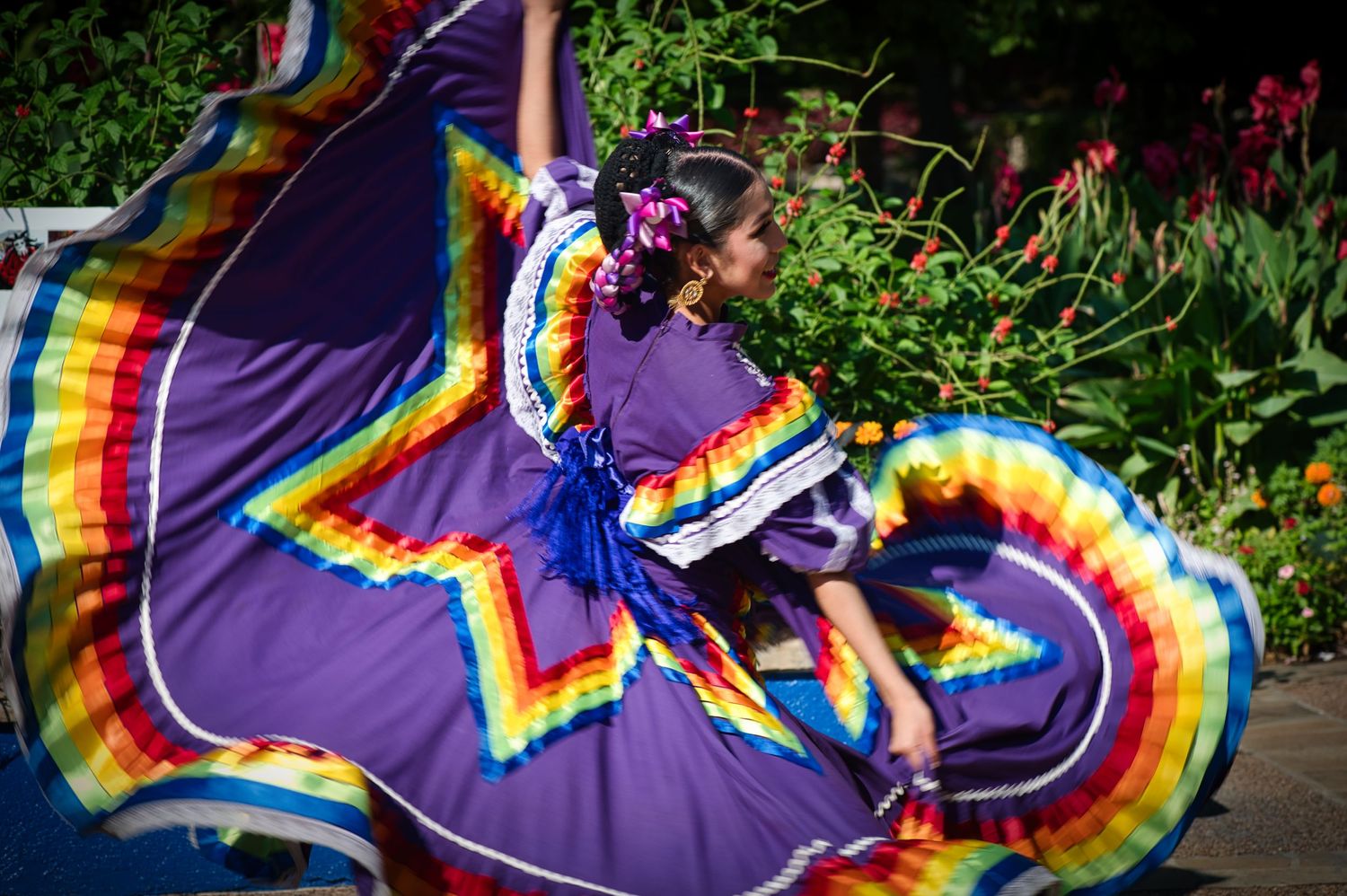 Dancer in flowing rainbow-colored traditional Mexican dress twirling during a performance.