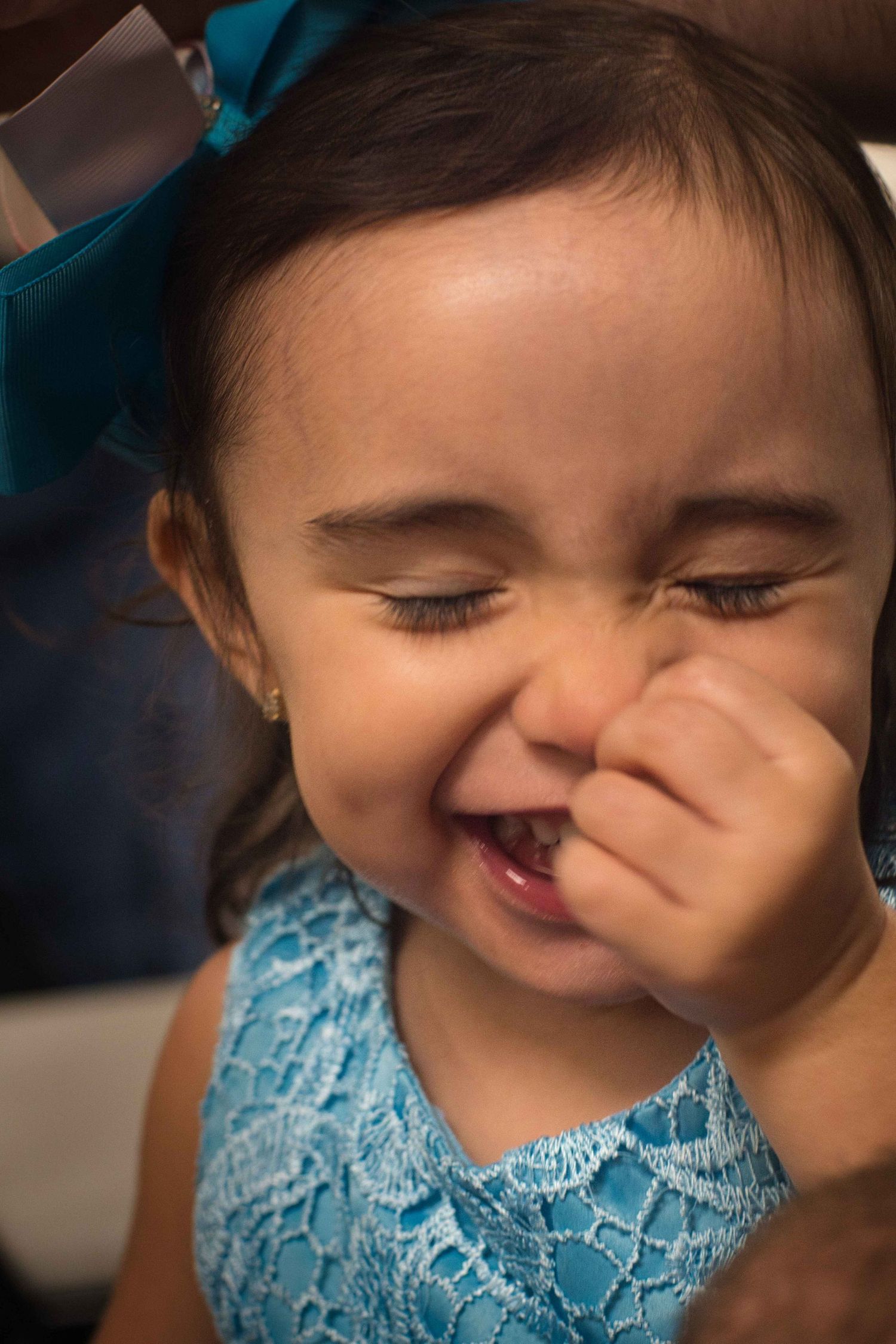 Child in blue lace dress laughing with hand covering face.