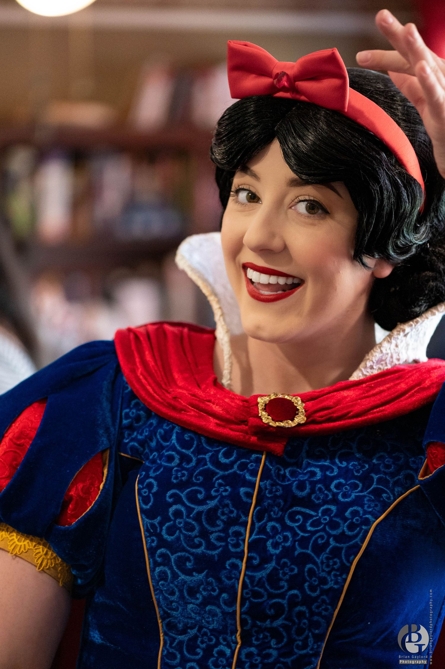 A character performer in a classic red, blue and gold princess costume with a red bow headband smiles warmly at the camera.