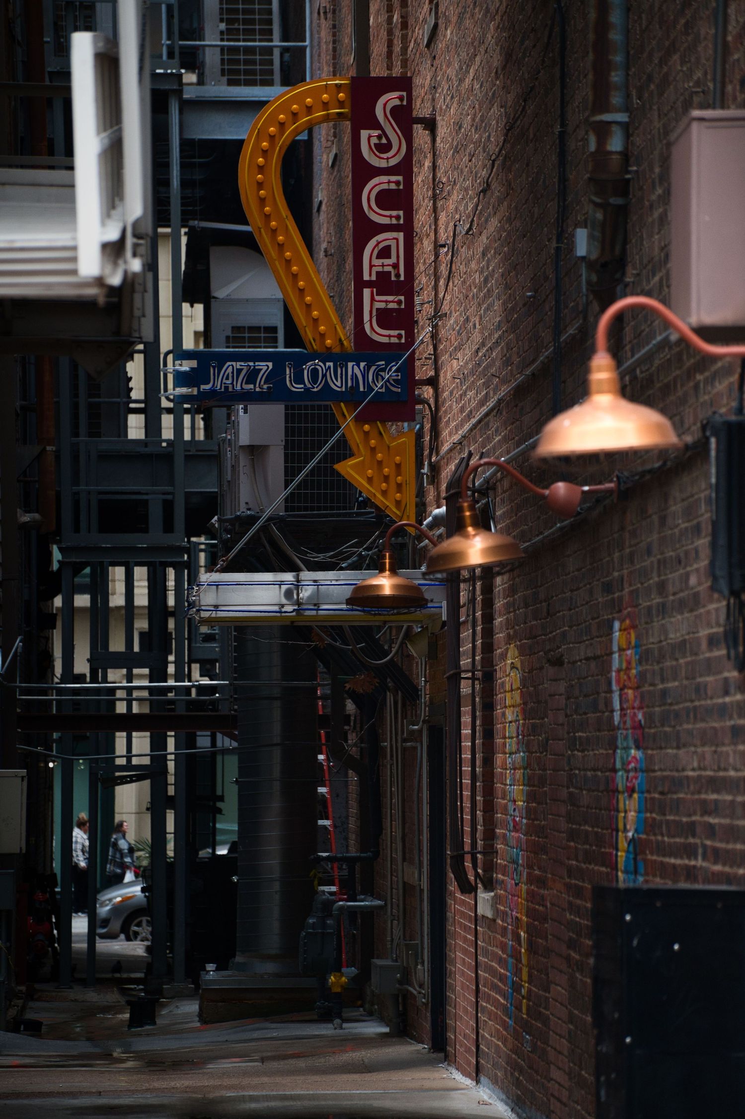 Vintage neon sign for a jazz lounge illuminates a brick alleyway at night.